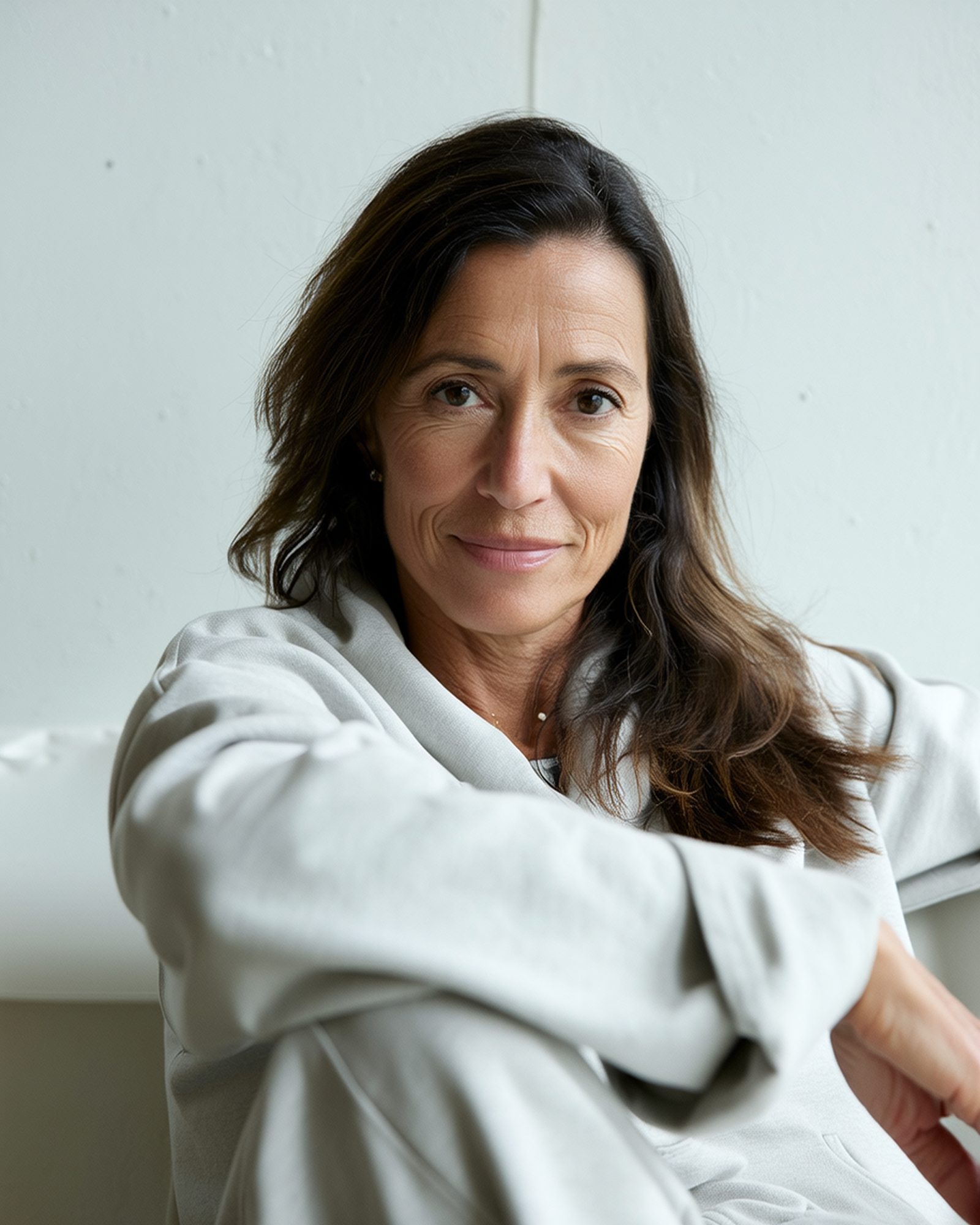 Vrouw van in de vijftig in een lichte kamer, kijkt rustig in de camera.